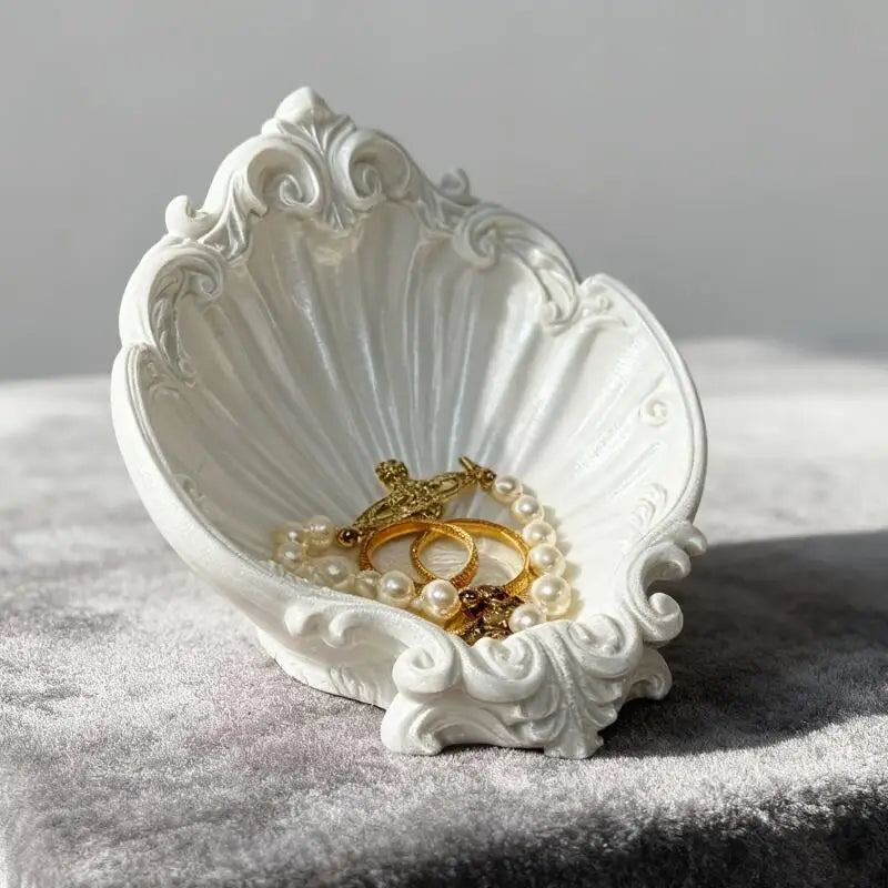 White vintage shell shaped jewelry tray holding gold jewelry on a gray velvet surface