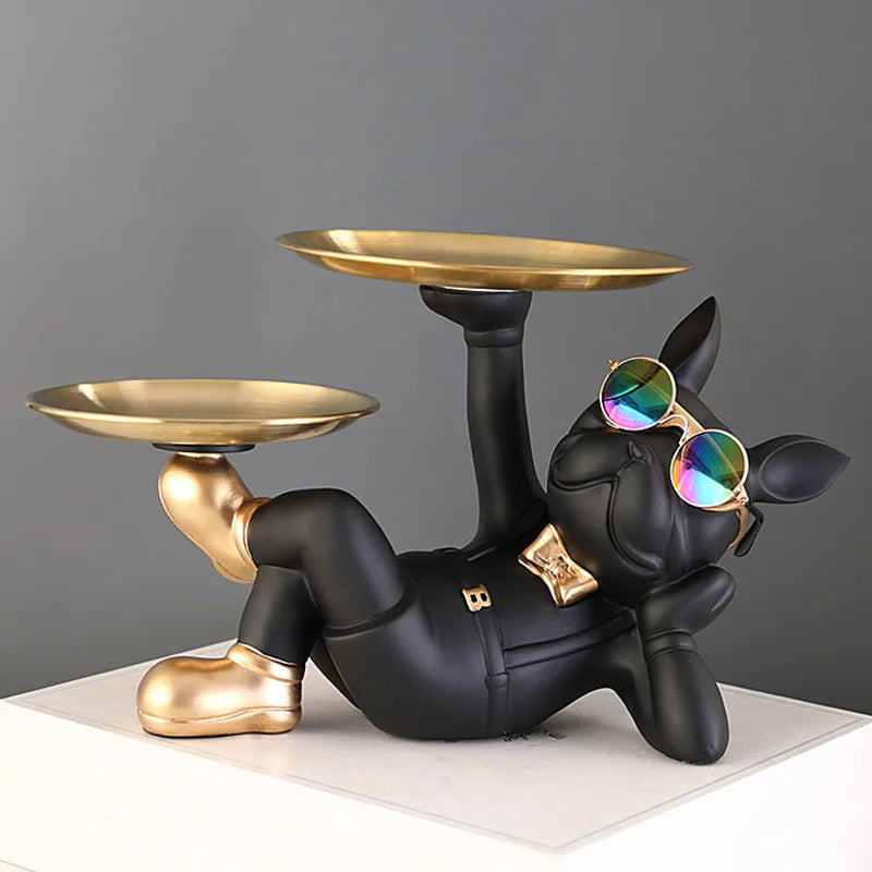 Black bulldog resin catchall sculpture with empty gold trays and sunglasses, on white tabletop