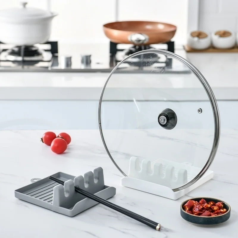 Grey and white utensil rests on a kitchen counter, one holding chopsticks, white one holding a pot lid