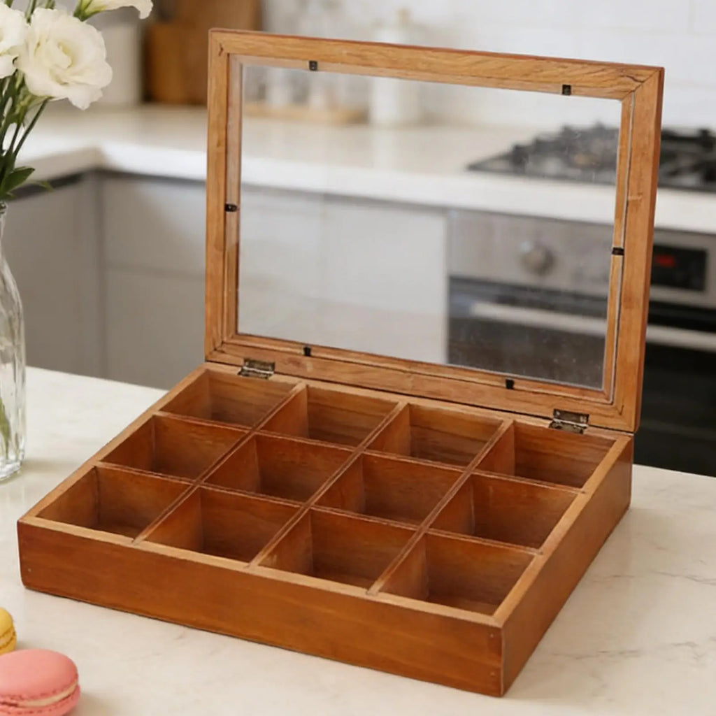 Wooden tea bag organizer with twelve empty compartments and a clear lid on a kitchen counter