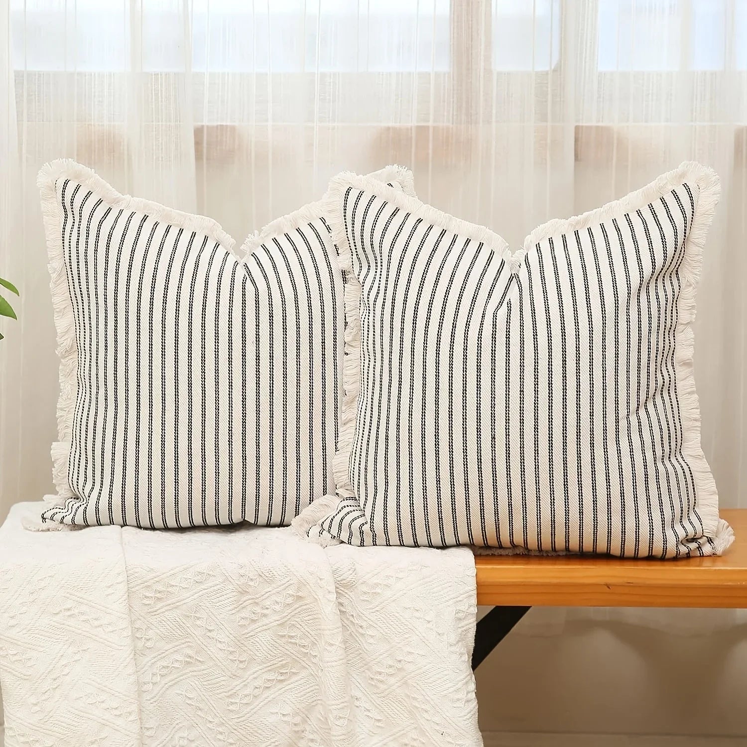 Pair of black striped throw pillow covers on a wooden bench in front of a window
