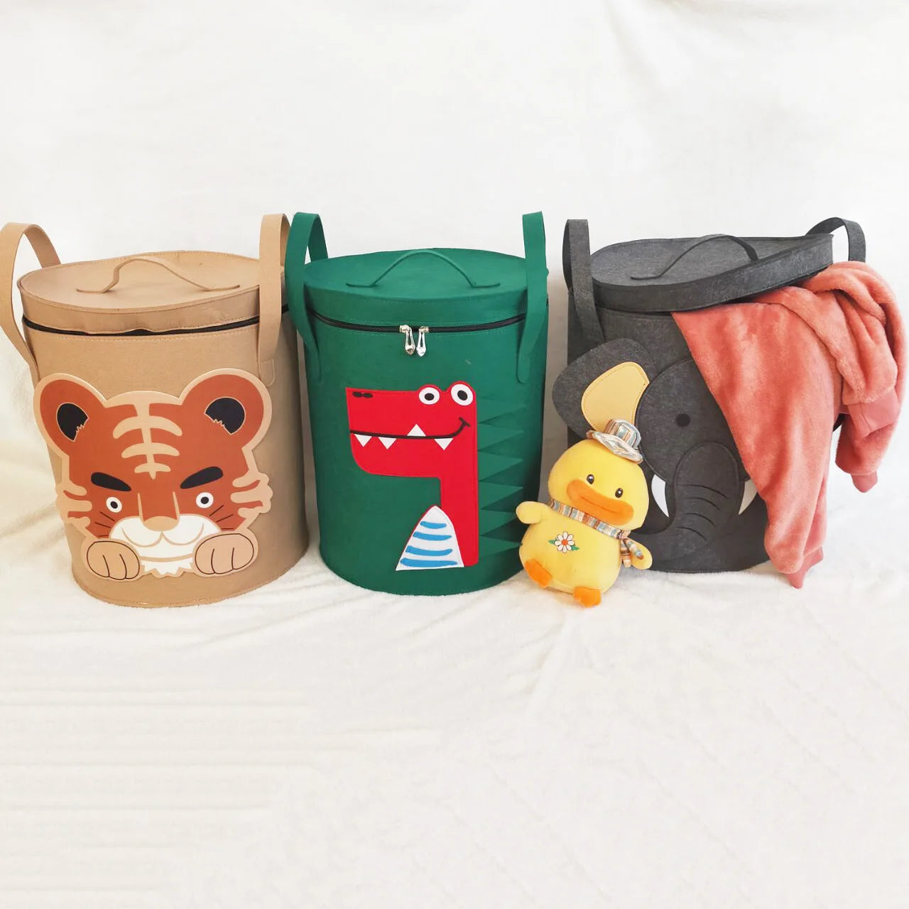 Three animal face storage baskets for toys, next to plush toys and a blanket