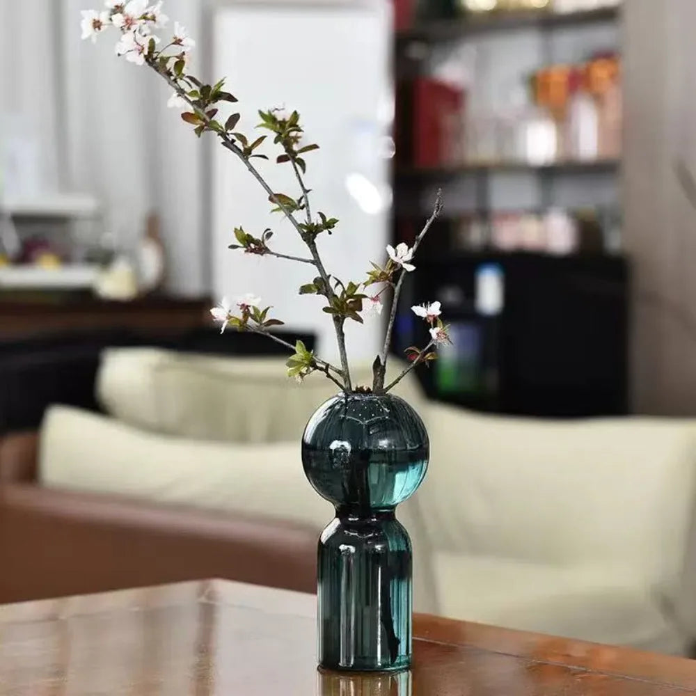 Teal striped glass vase with round globe detail holding a branch with blossoms on a wooden table
