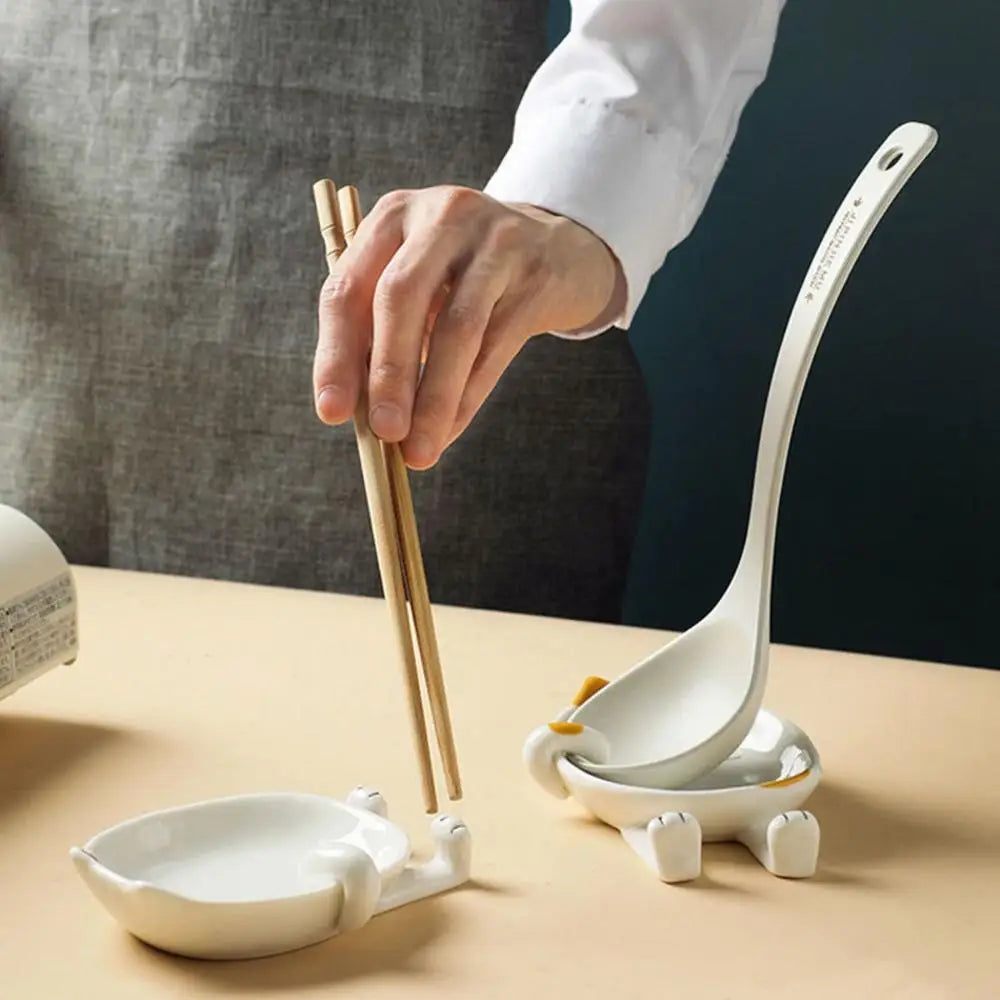 Hand placing chopsticks on a ceramic cat spoon rest beside a ladle holder