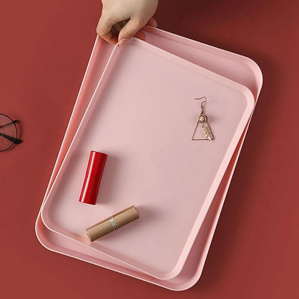 Hand holding a stack of two pink matte trays with small items like a lipstick and earring, against a red background.