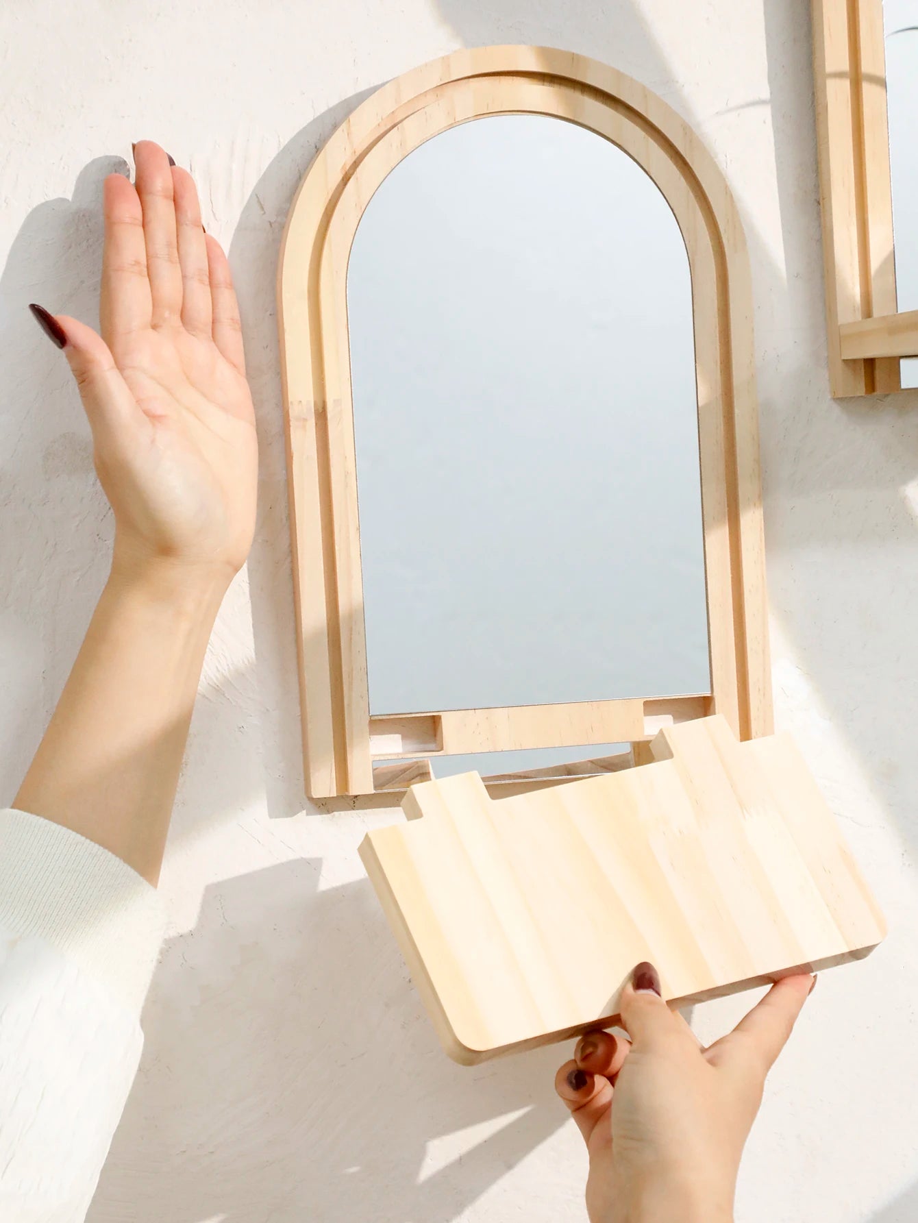 close-up of the removable shelf being attached to the wooden arched mirror frame, showing assembly