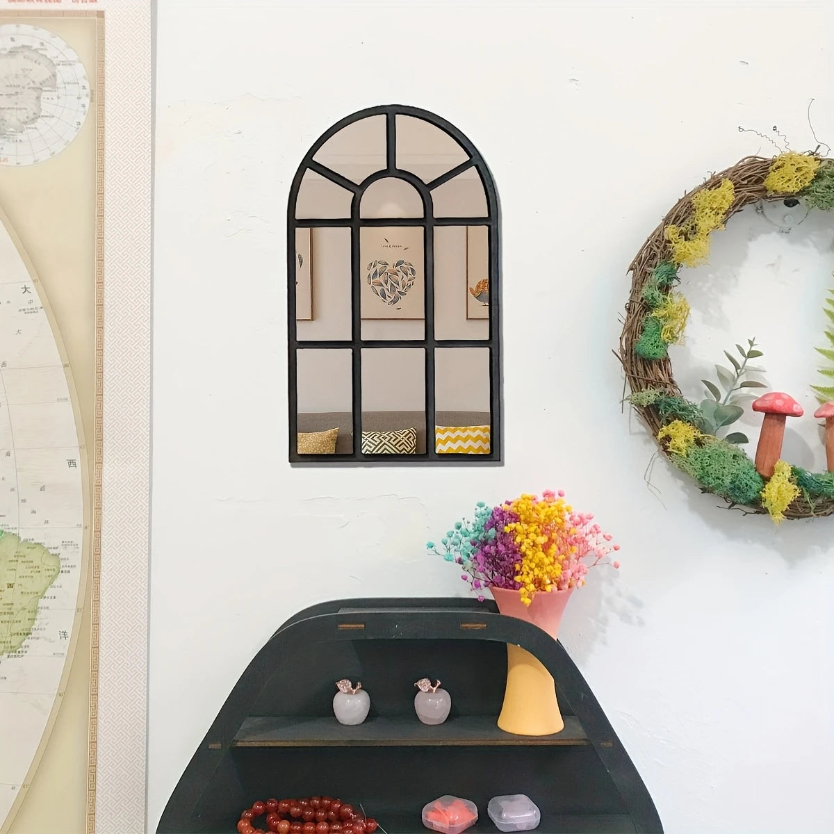 Rounded arch windowpane wall mirror with a black frame hanging on a white wall above a decorative shelf and wreath
