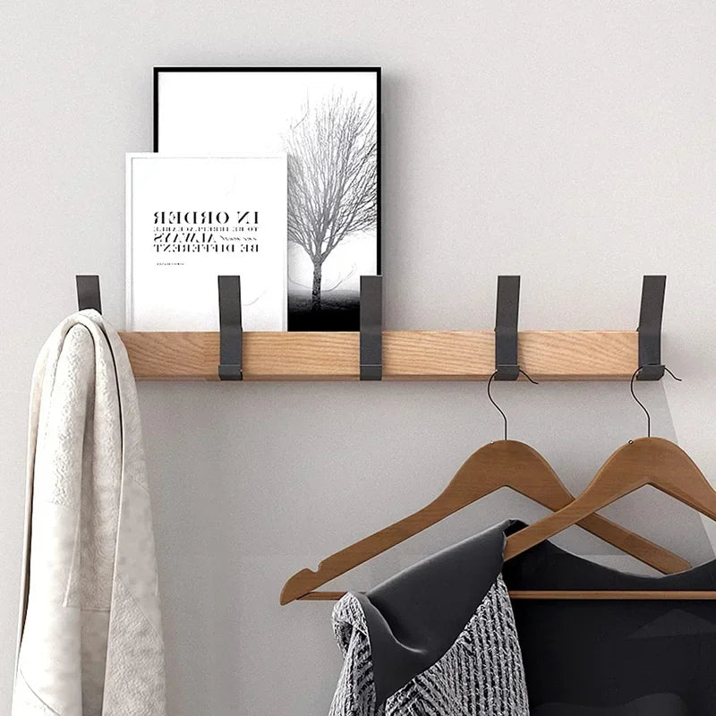 oak coat rack with five hooks mounted on wall, holding hangers, coat, and frames