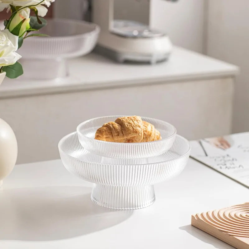 Two ribbed glass pedestal bowls on a counter, one large and one small, with a croissant