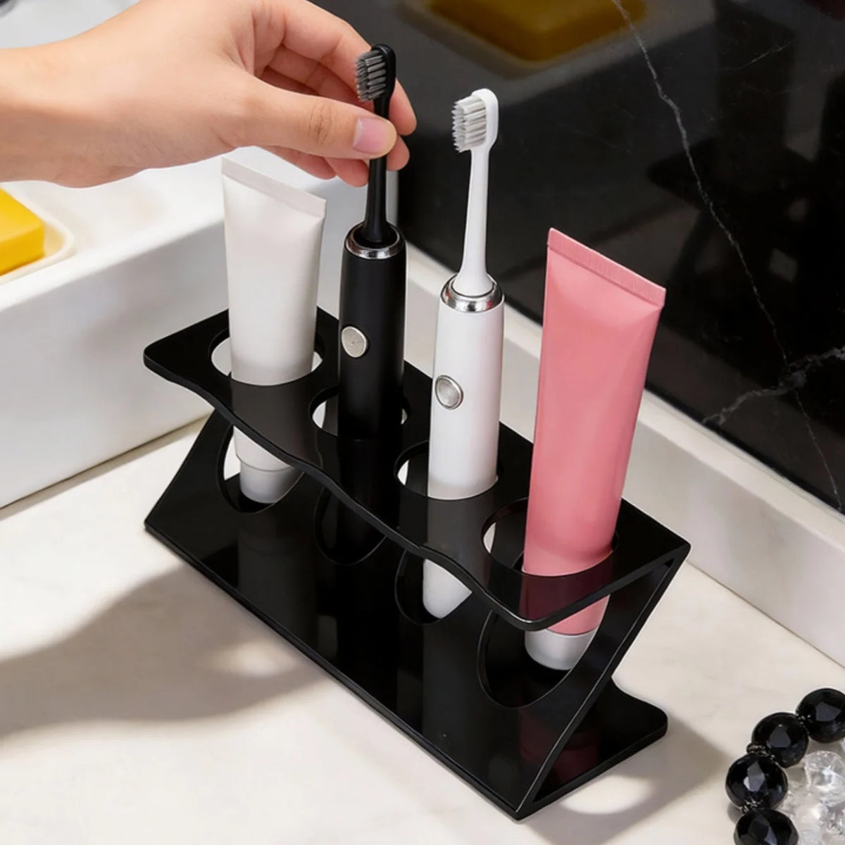 Hand placing a black electric toothbrush into a black ventilated bathroom organizer with tubes and other brushes