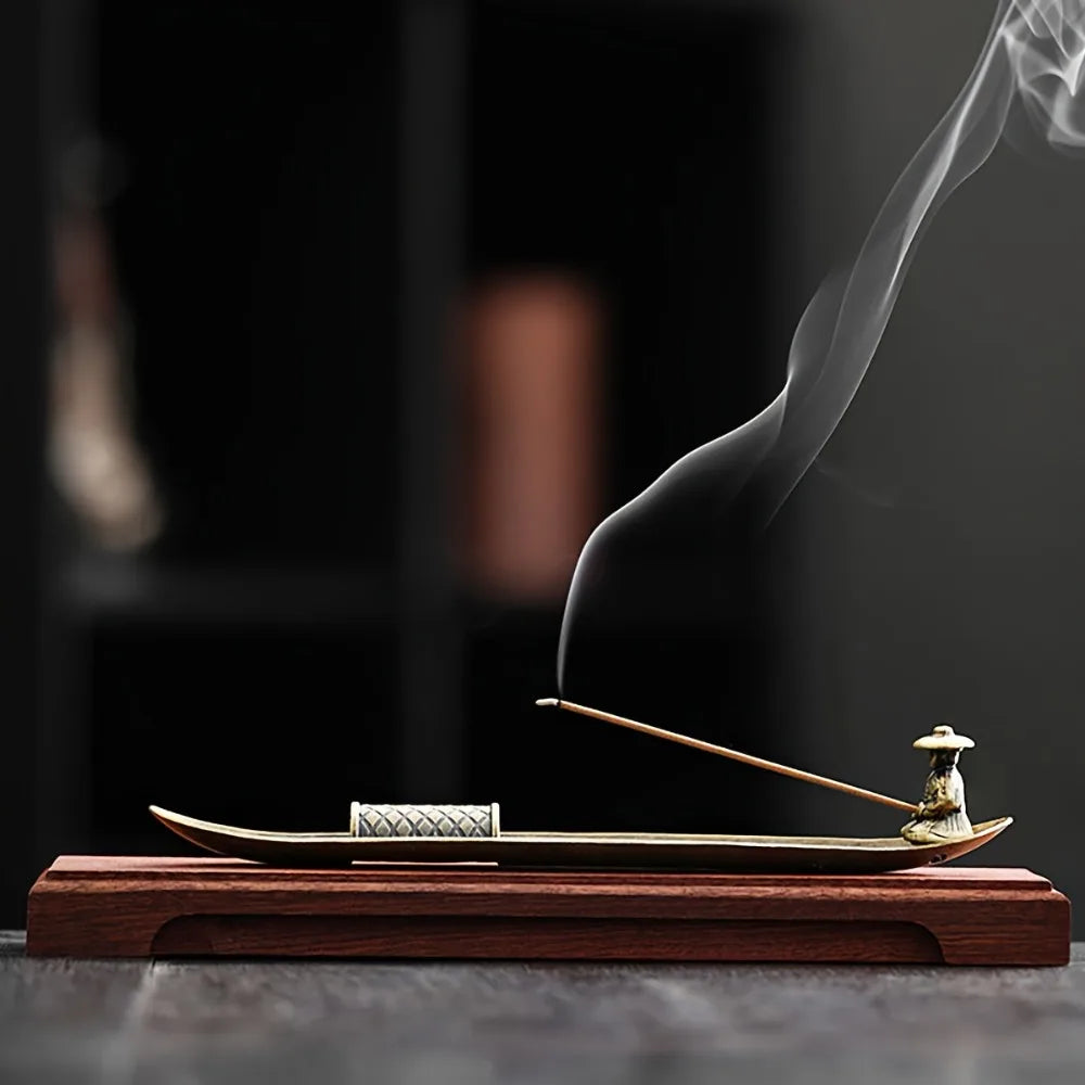 Japanese-style metal incense holder in boat form with incense stick, displayed on wooden base
