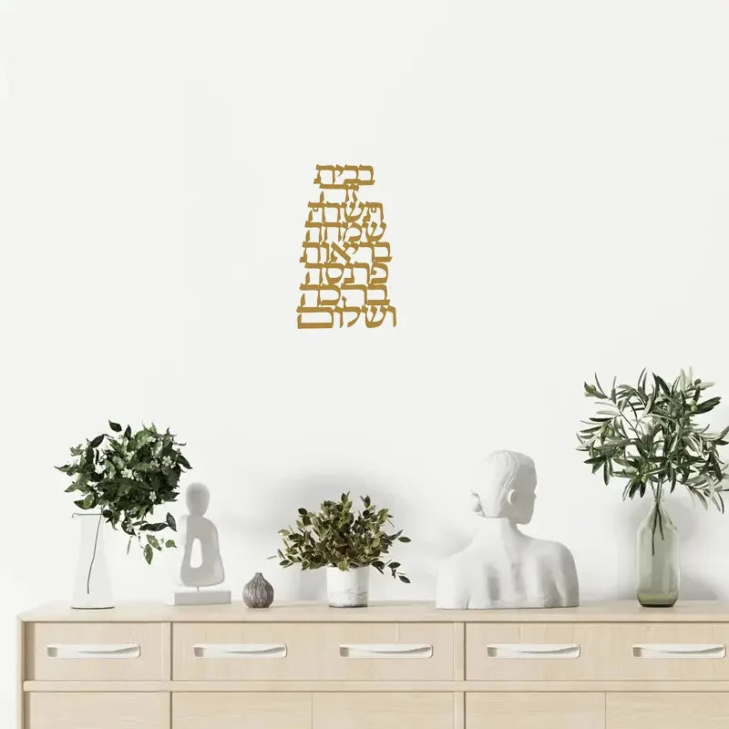 Modern gold Hebrew letter metal wall art styled above a dresser with decorative plants and abstract sculpture