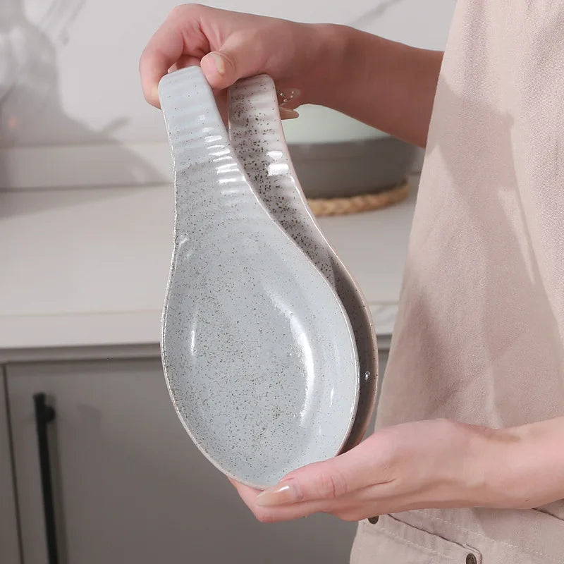 Person holding two stacked gray speckled ceramic spoon rests in their hand
