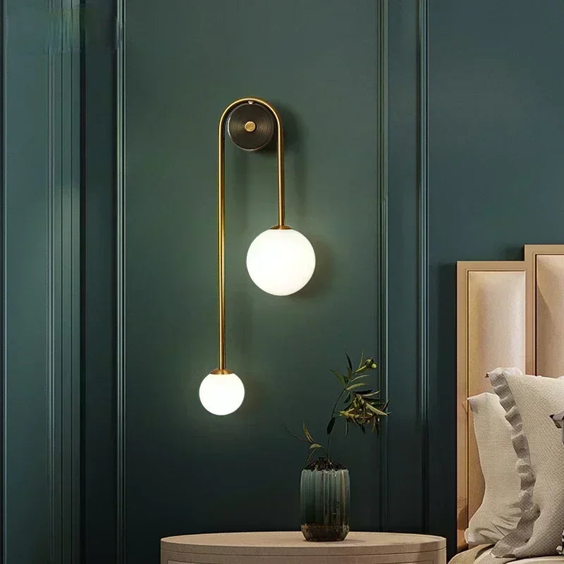 Gold and glass globe wall sconce styled above a nightstand in a bedroom with green walls