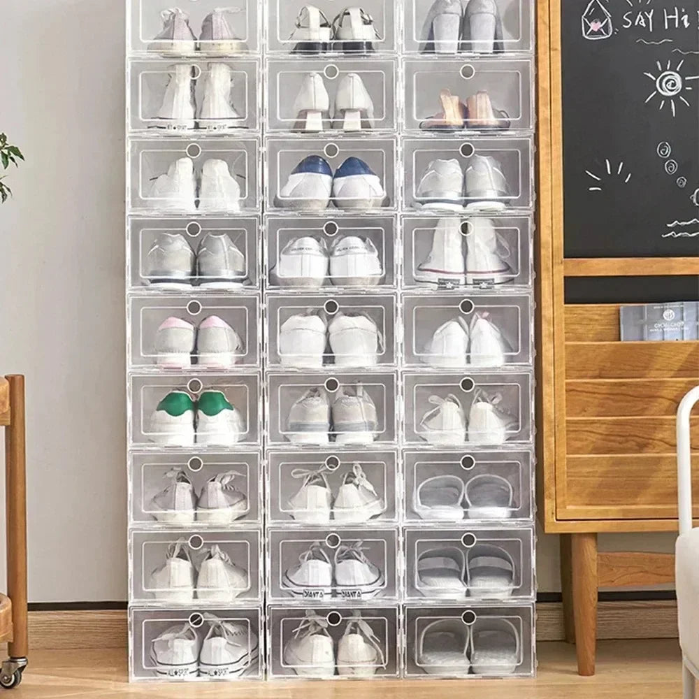 Tall stack of clear shoe boxes filled with various shoes in a modern interior next to a dresser and chalkboard wall