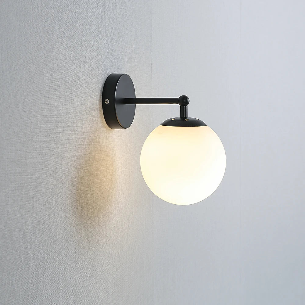 Single globe wall sconce with black finish and frosted glass shade on wall