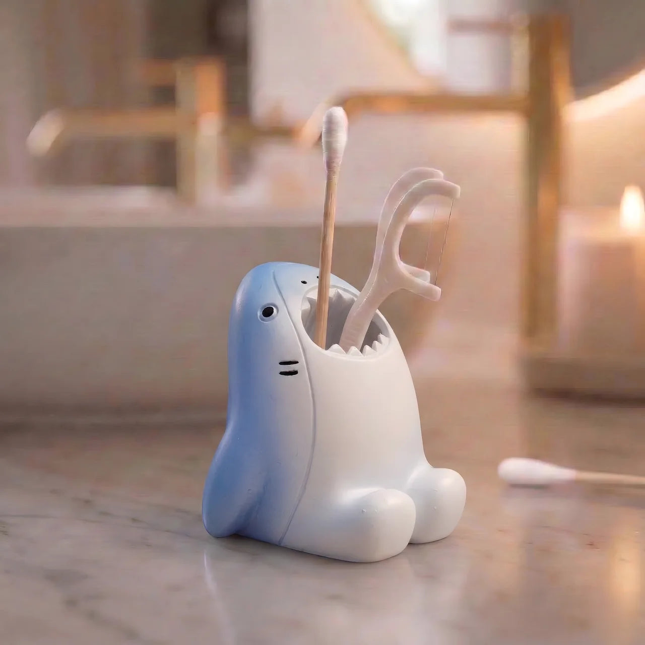 Blue and white shark-shaped toothbrush holder on a bathroom vanity holding cotton swabs and a floss pick.