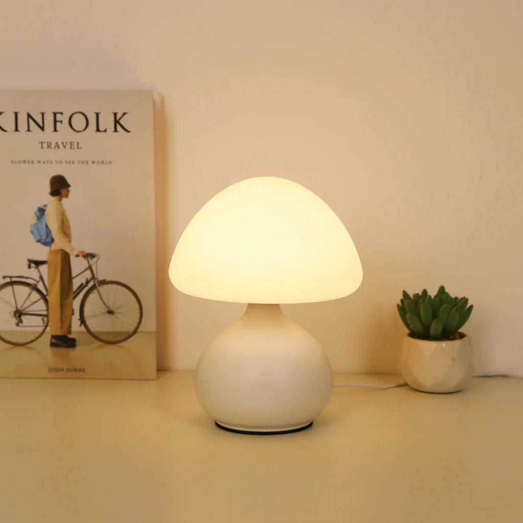 White mushroom table lamp glowing on a nightstand beside a book and succulent