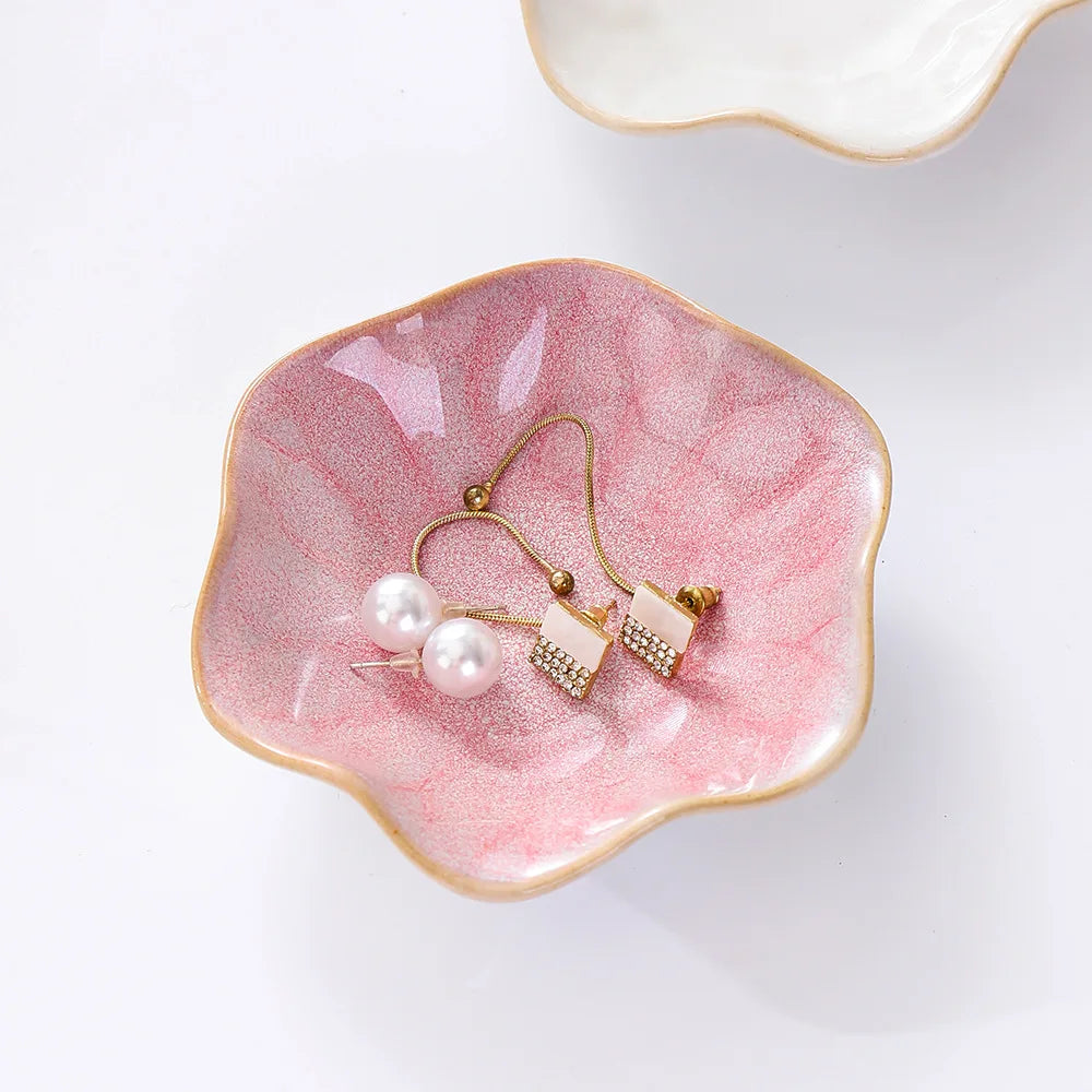 Pink ceramic petal edge jewelry tray holding pearl earrings on a white background