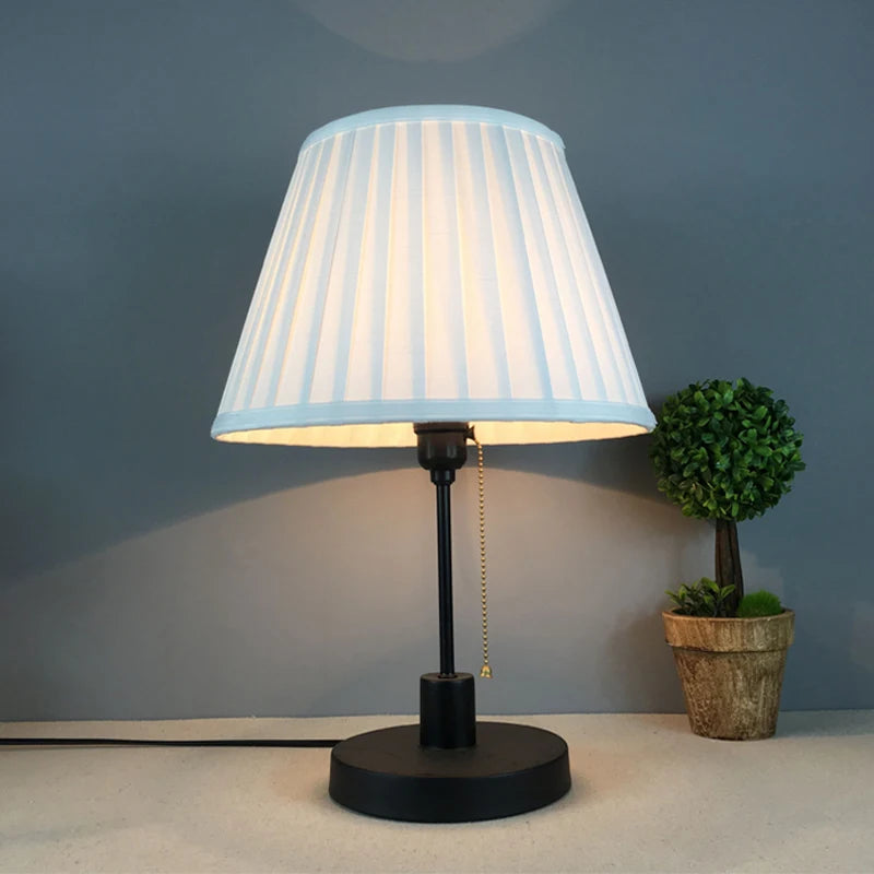 White pleated fabric lampshade fitted on a black metal desk lamp
