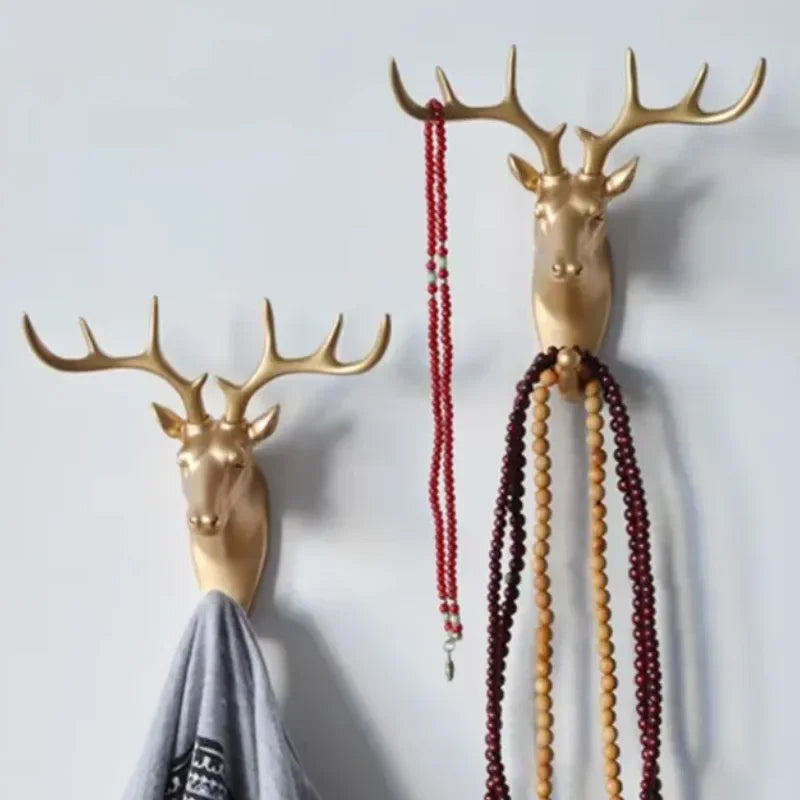 Two gold deer head wall hooks mounted on the wall, each holding necklaces and a shirt