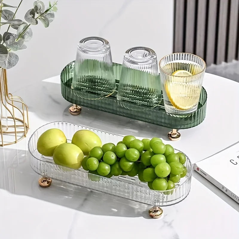 Clear and green acrylic trays with gold feet holding fruit and glasses, shown on a light tabletop for decorative home use