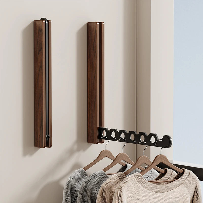 Foldable wall-mounted walnut drying rack with hangers holding clothes in a modern room