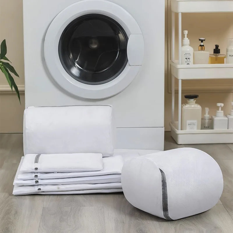 Set of various white mesh laundry bags arranged in front of a washing machine