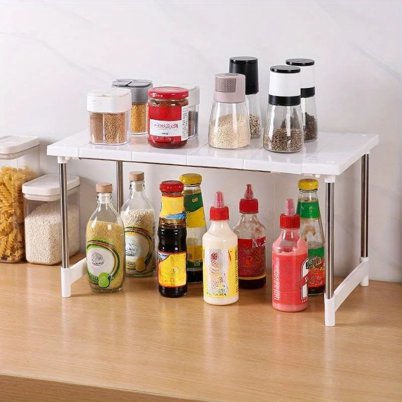 White expandable kitchen shelf organizing spices, oils, and condiments on a countertop