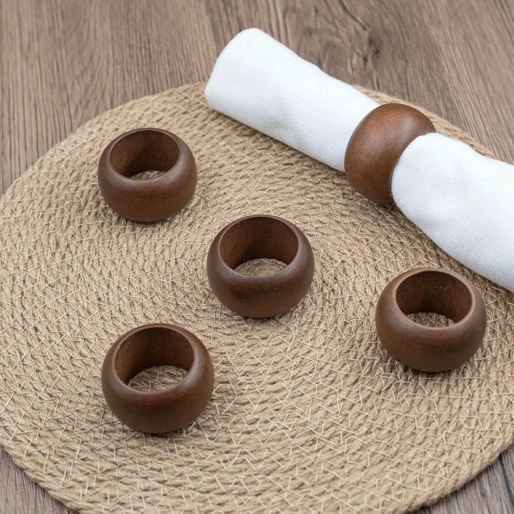 Round acacia wood napkin rings displayed on woven placemat, one holding a folded white napkin