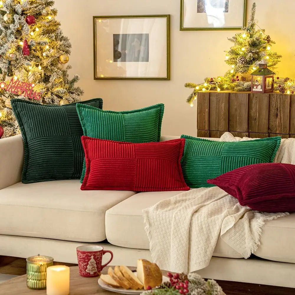 Assorted red and green corduroy pillow covers styled on a cream sofa in a festive living room scene with Christmas decor