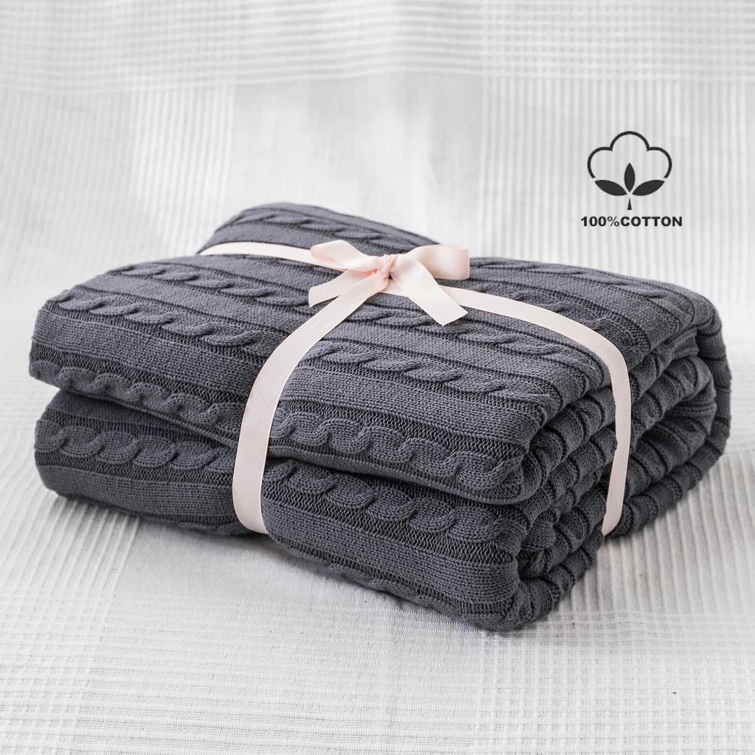dark grey cable knit cotton throw blanket neatly folded with ribbon on white background