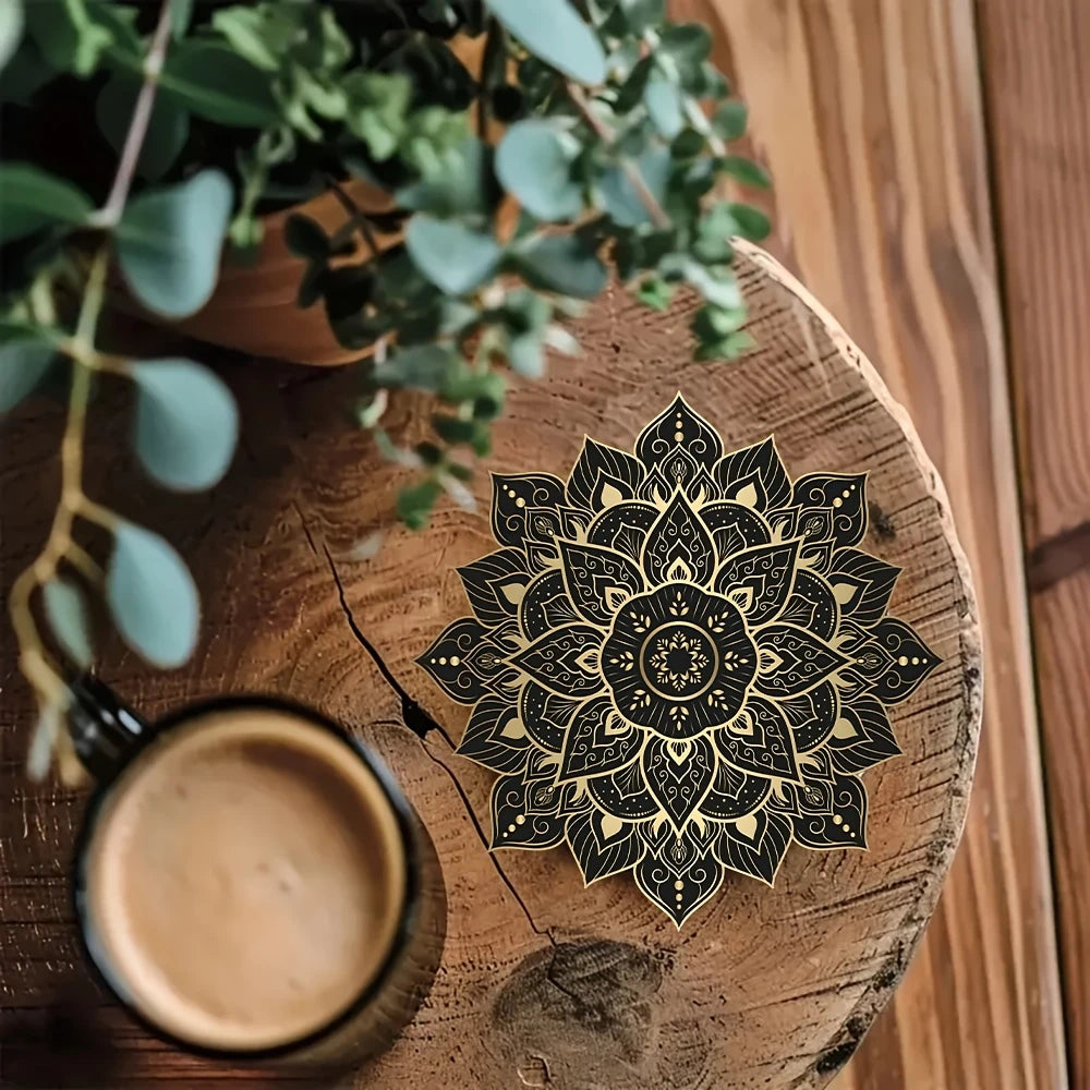 Single black and gold mandala flower coaster on a rustic wooden table with a coffee mug and plant