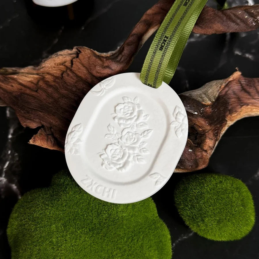 Single white floral gypsum stone hanging diffuser with green ribbon resting on driftwood and moss