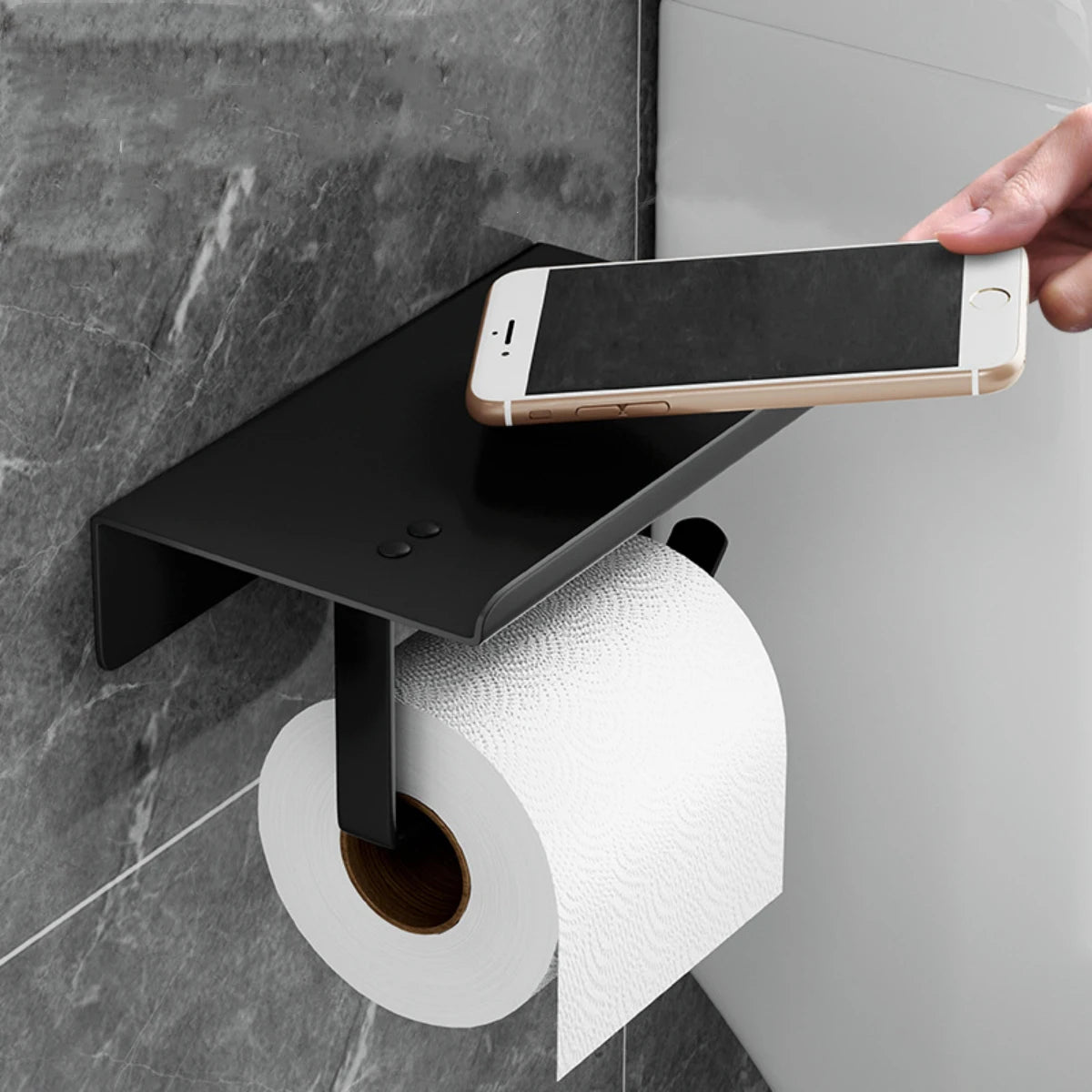Black stainless steel wall-mounted toilet paper holder with flat shelf, hand placing a smartphone on top