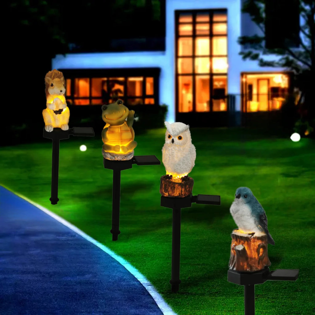 Four animal-shaped solar pathway lights (squirrel, frog, owl, bird) glowing along a yard walkway at night