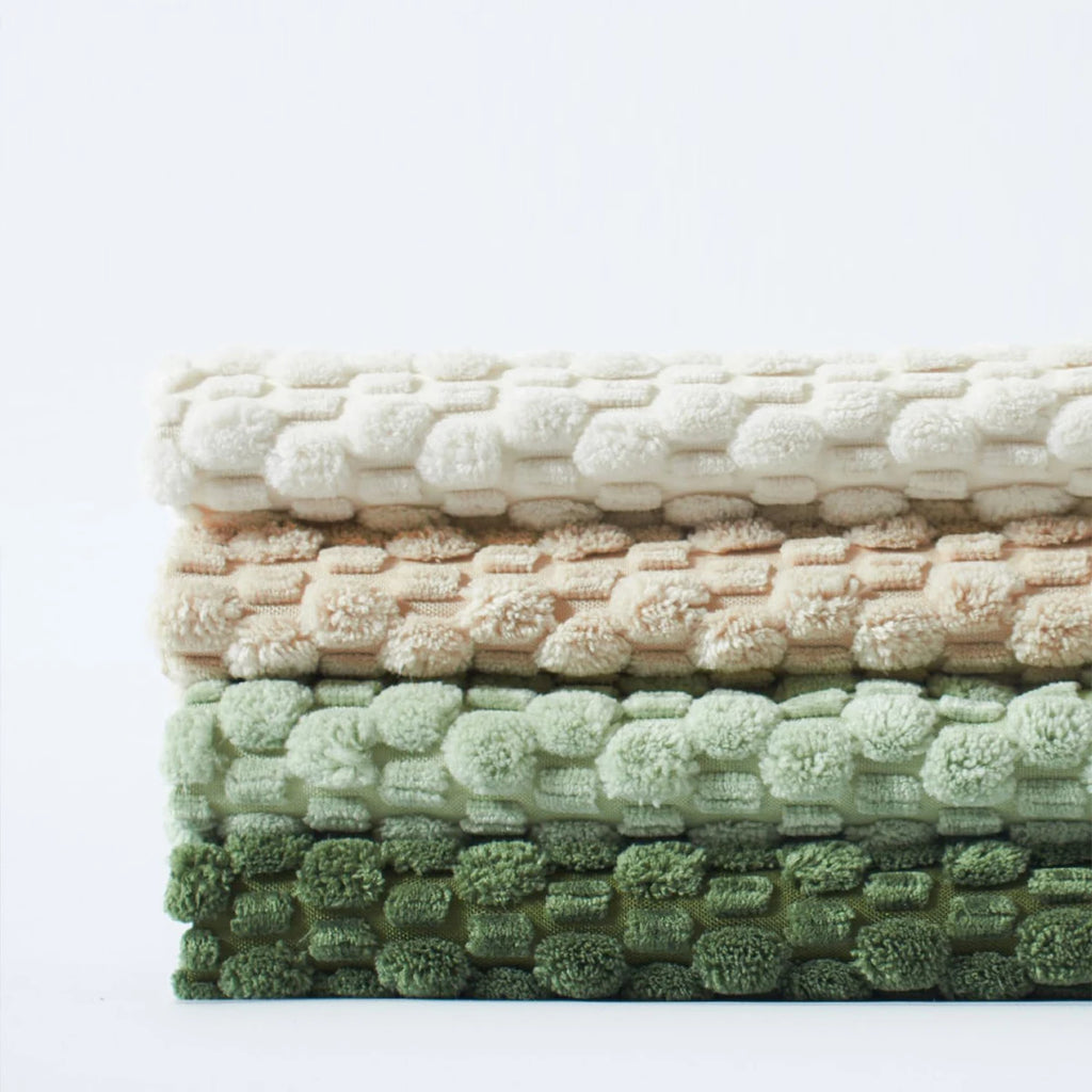 A neatly folded stack of four textured corduroy pillow covers in white, beige, light green, and dark green, highlighting the thickness and fabric detail