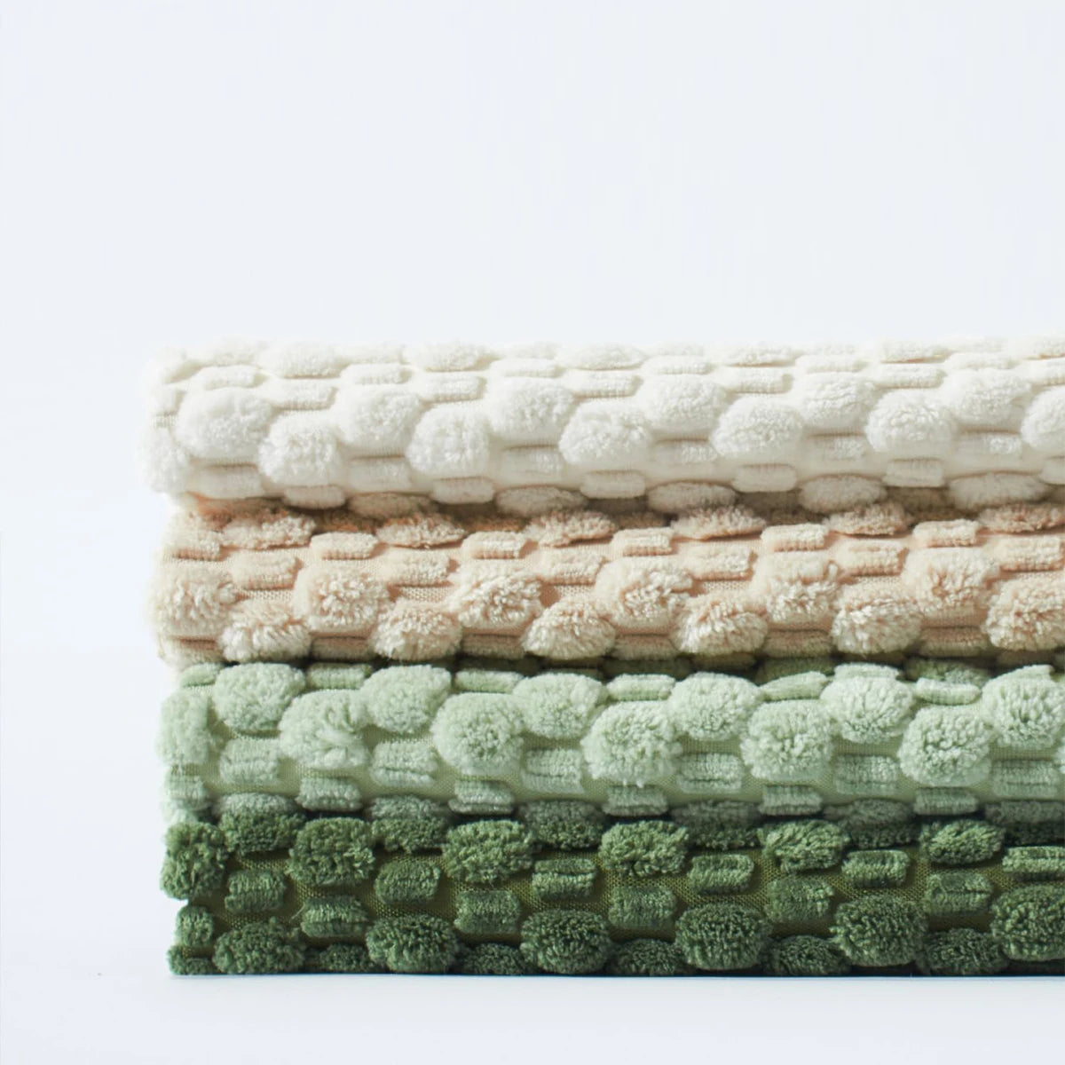 A neatly folded stack of four textured corduroy pillow covers in white, beige, light green, and dark green, highlighting the thickness and fabric detail