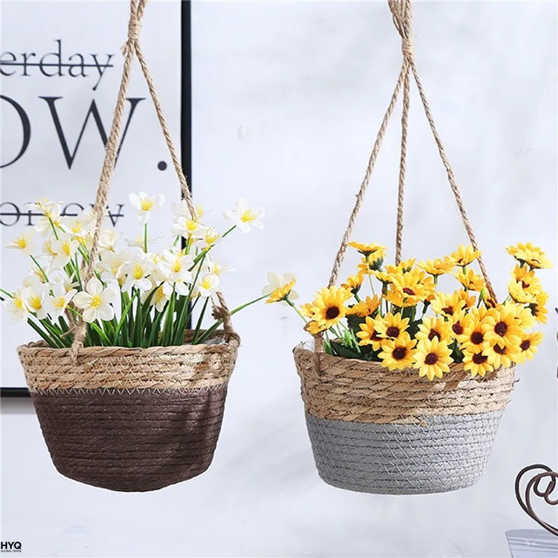 Two woven jute hanging baskets, one with brown and one with grey base, each filled with artificial yellow and white flowers, displayed against a light wall
