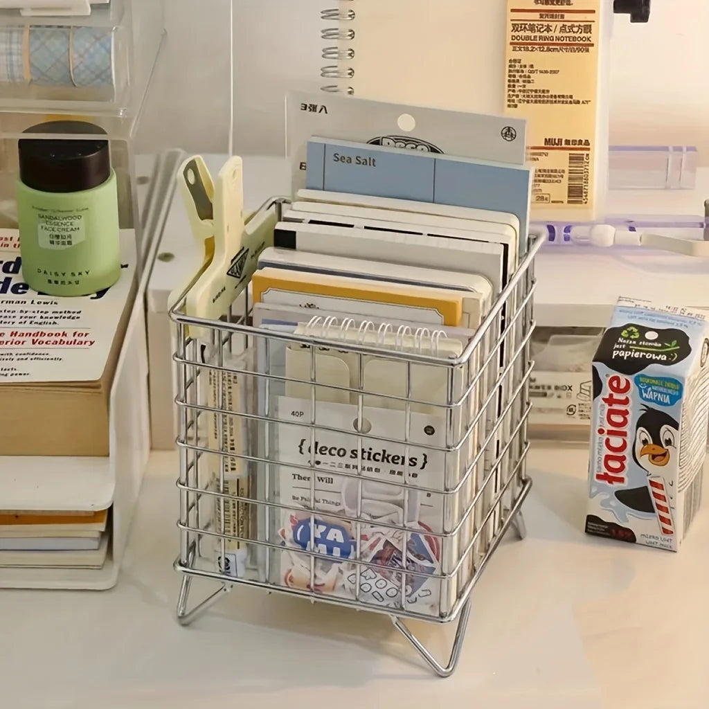 Silver metal grid basket holding notebooks, stickers, and supplies on a desk