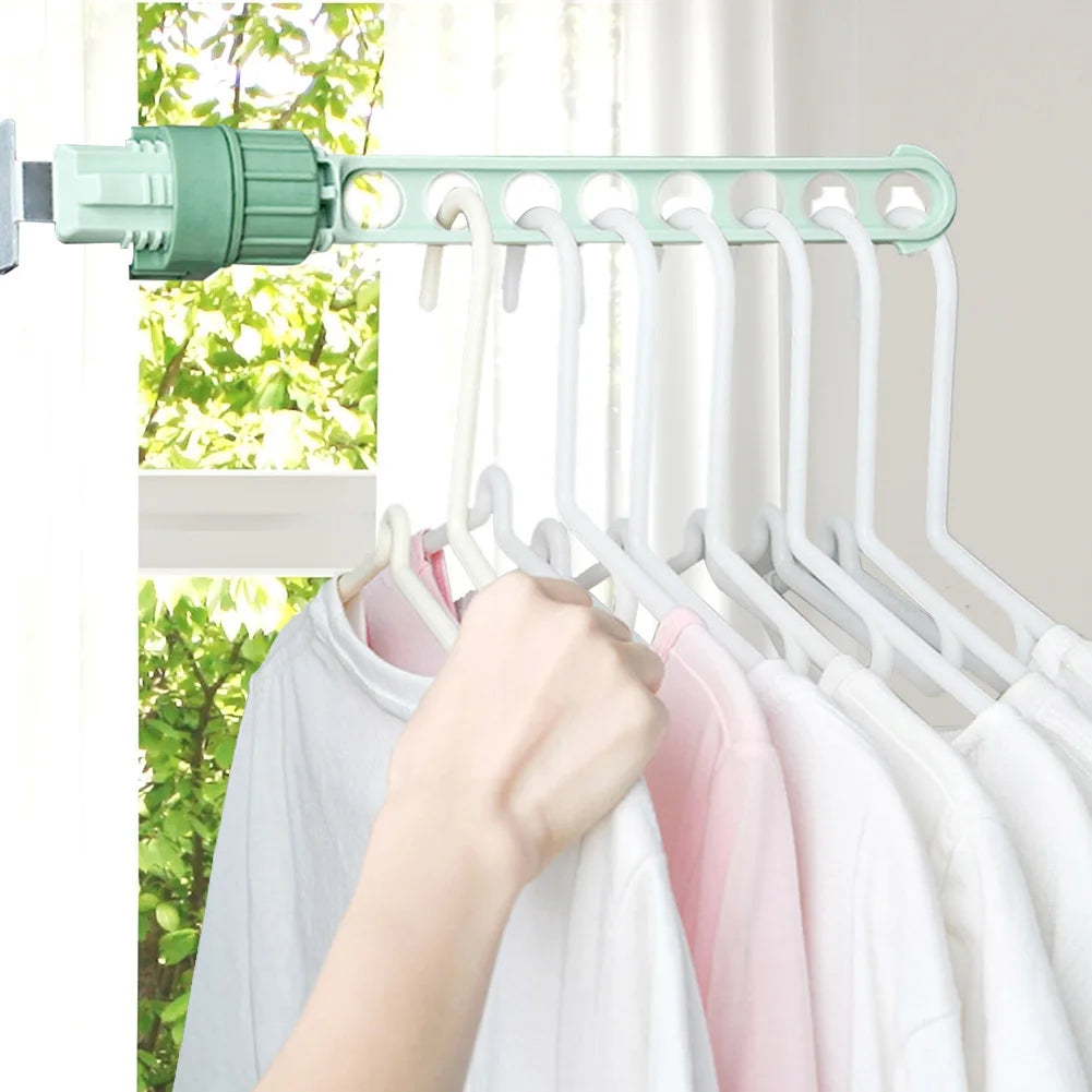 Green wall-mounted drying rack holding several shirts on hangers in front of a sunny window with greenery outside.