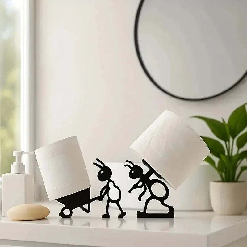 Ant silhouette tissue roll holders displayed together on a bathroom counter, each holding a toilet paper roll with one ant pushing a wheelbarrow and the other carrying a roll.