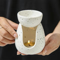 Person holding a white speckled ceramic essential oil burner with a lit tealight inside