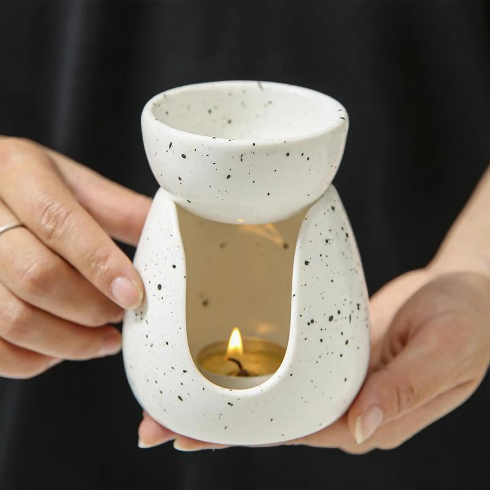 Person holding a white speckled ceramic essential oil burner with a lit tealight inside