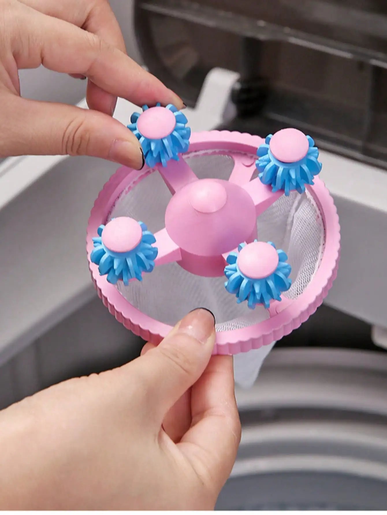 Hand placing a pink lint catcher ball with blue rollers into a washing machine