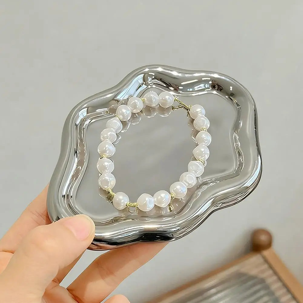 Hand holding a small silver cloud jewelry tray with a beaded bracelet