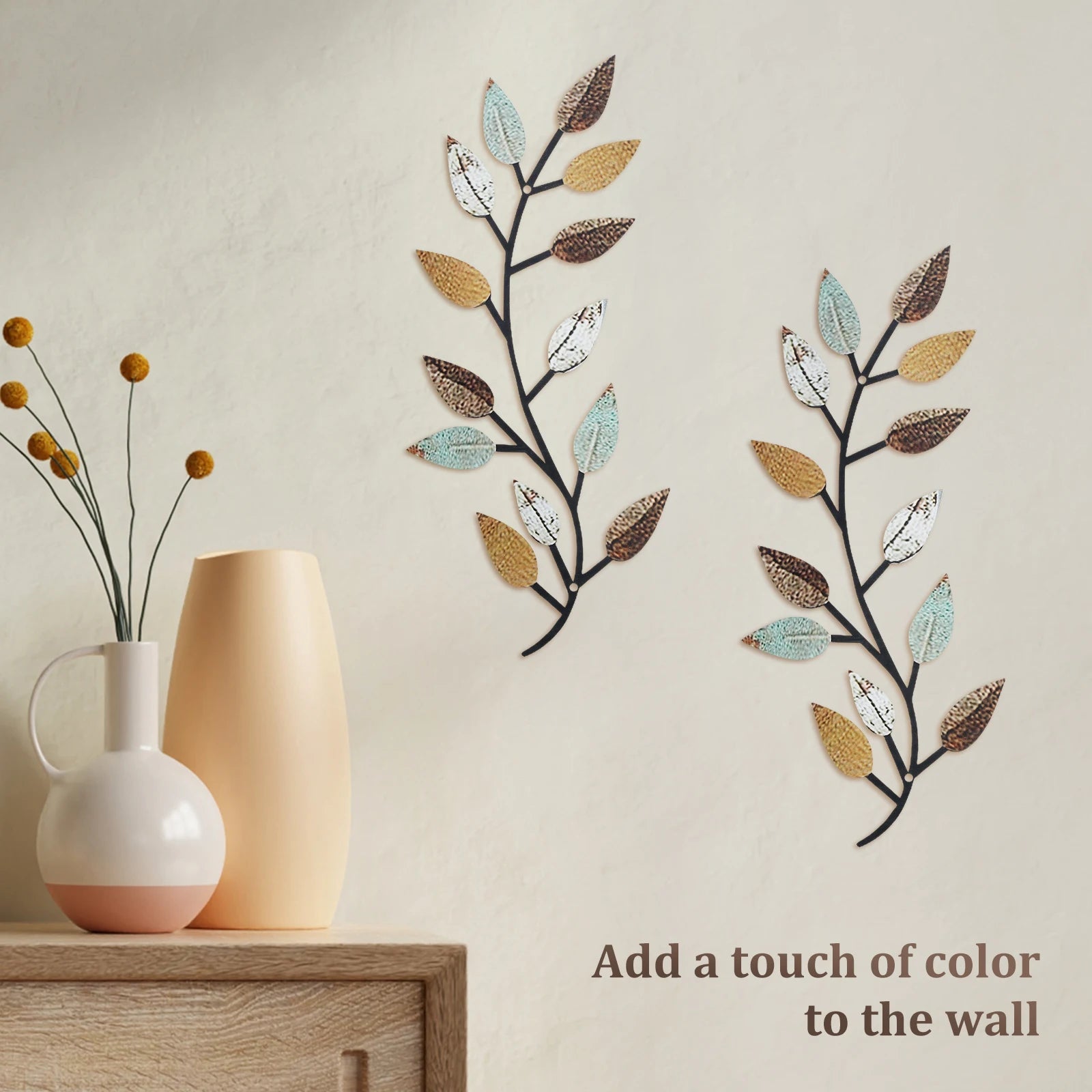 Set of two olive branch metal wall art pieces with colored leaves on a neutral wall, styled above a console with vases