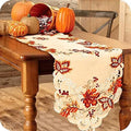 Maple leaf embroidered fall table runner on a wooden dining table with autumn pumpkins