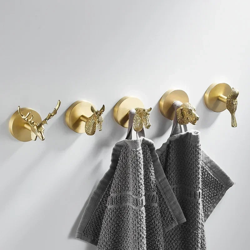 Five brass animal wall hooks lined up on a white wall with gray towels hanging