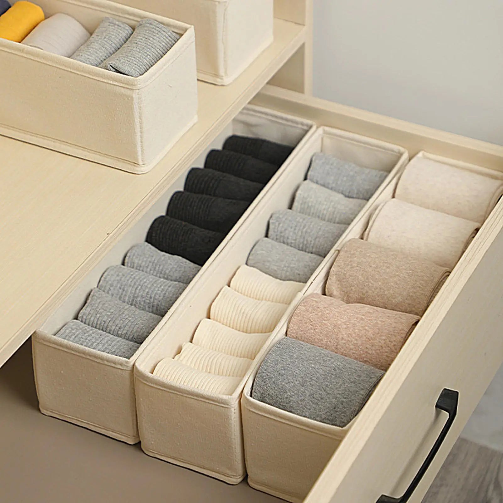 Three slim beige fabric organizer bins lined in a drawer with socks and undergarments sorted by color